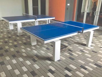 Two blue table tennis tables are set up indoors on a tiled floor.