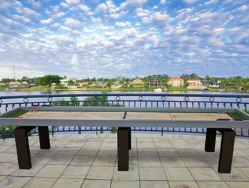 Long wooden bench on tiled balcony overlooking waterfront with houses and cloudy sky.