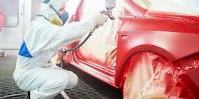 Person in protective gear spray-painting a red car.
