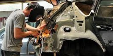 A person welding a damaged car frame in a workshop.