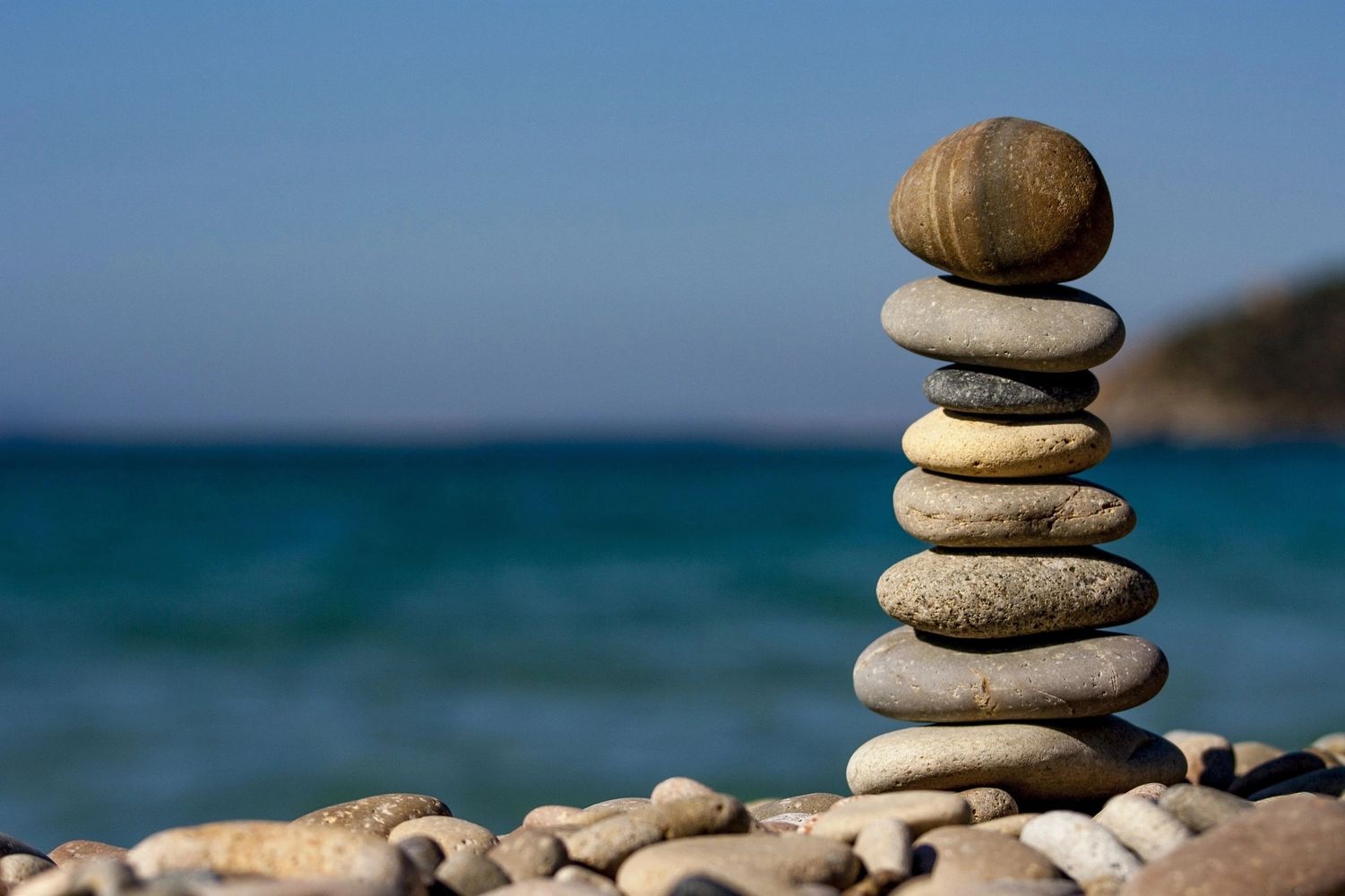 Stacked stones balanced by the seaside with a clear blue sky.
