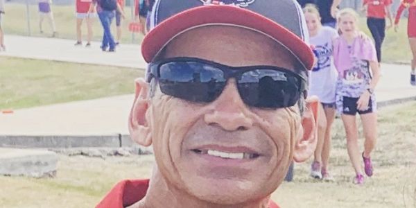 Smiling man wearing sunglasses and a cap outdoors.