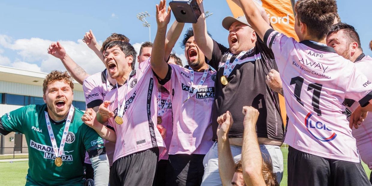 Soccer team celebrating victory with medals and trophy on a sunny day.