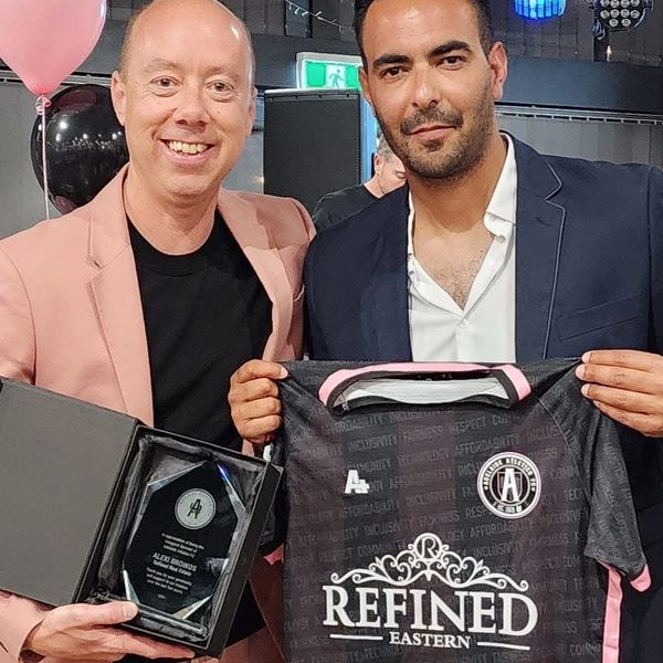 Two men holding an award plaque and a football jersey with 'Refined Eastern' branding.