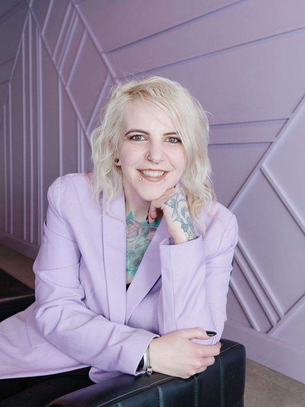 Smiling woman with blonde hair in a lavender blazer.