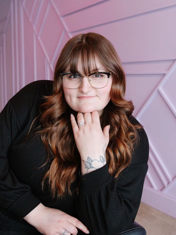 Young woman with glasses smiling against a pastel wall.