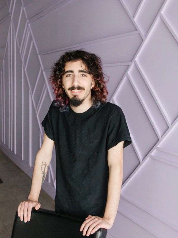 Young man with curly hair smiling and leaning on a chair.
