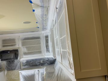 Kitchen cabinets and surfaces covered in plastic for painting preparation.