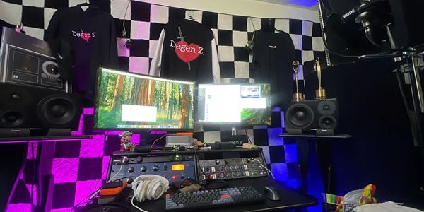 Audio workstation with dual displays, studio monitors, acoustic panels, and purple lighting.
