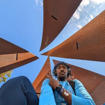 Person sitting below tall, triangular structures under a blue sky.