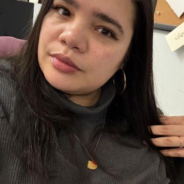 Young woman with long dark hair wearing hoop earrings and a pendant necklace.
