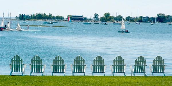 Empty chairs facing a calm lake with sailing boats.
