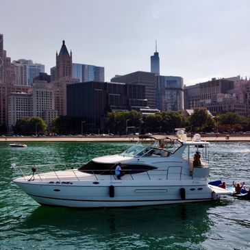 A yacht with people relaxing on a lake near a city skyline.