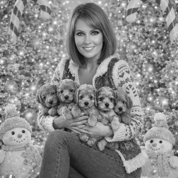 Woman in festive attire holding five puppies with holiday decorations around.