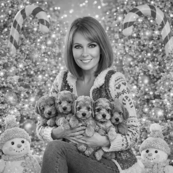 Woman holding five puppies with Christmas decorations.