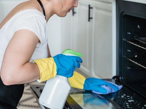 House cleaner wiping the interior of a oven door with cloth and household cleaner