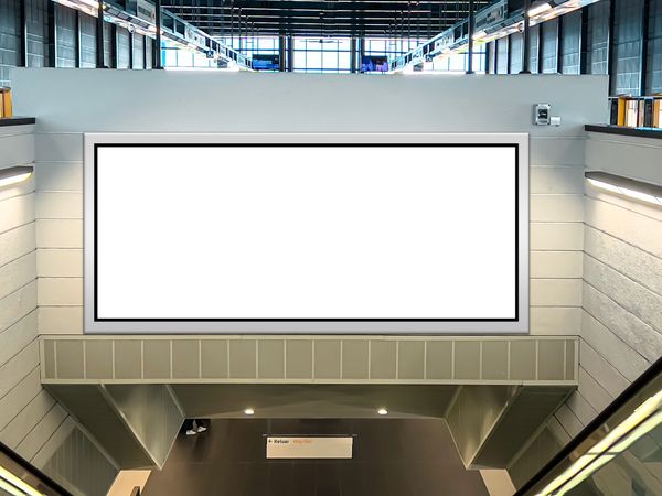 A large blank advertisement display is mounted on a wall in a modern, spacious public area