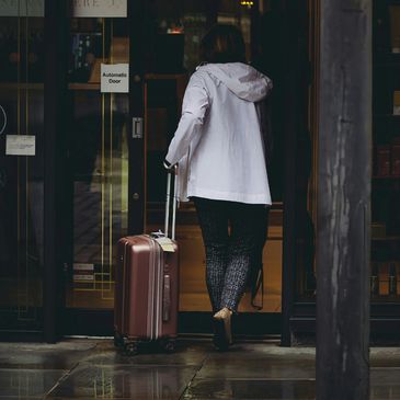 Person entering a building with rolling suitcase in rainy weather.