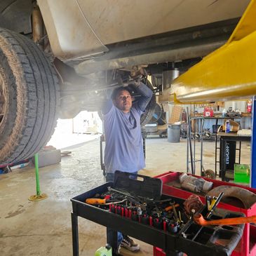 Mechanic working under a lifted vehicle in a garage.