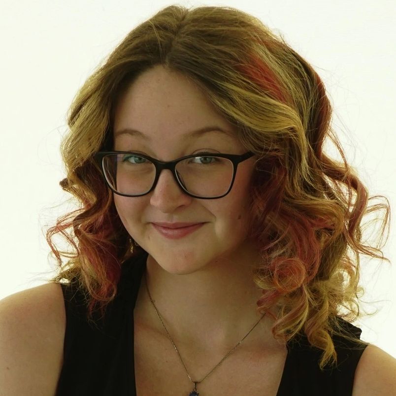 Young woman with curly hair and glasses smiling warmly.