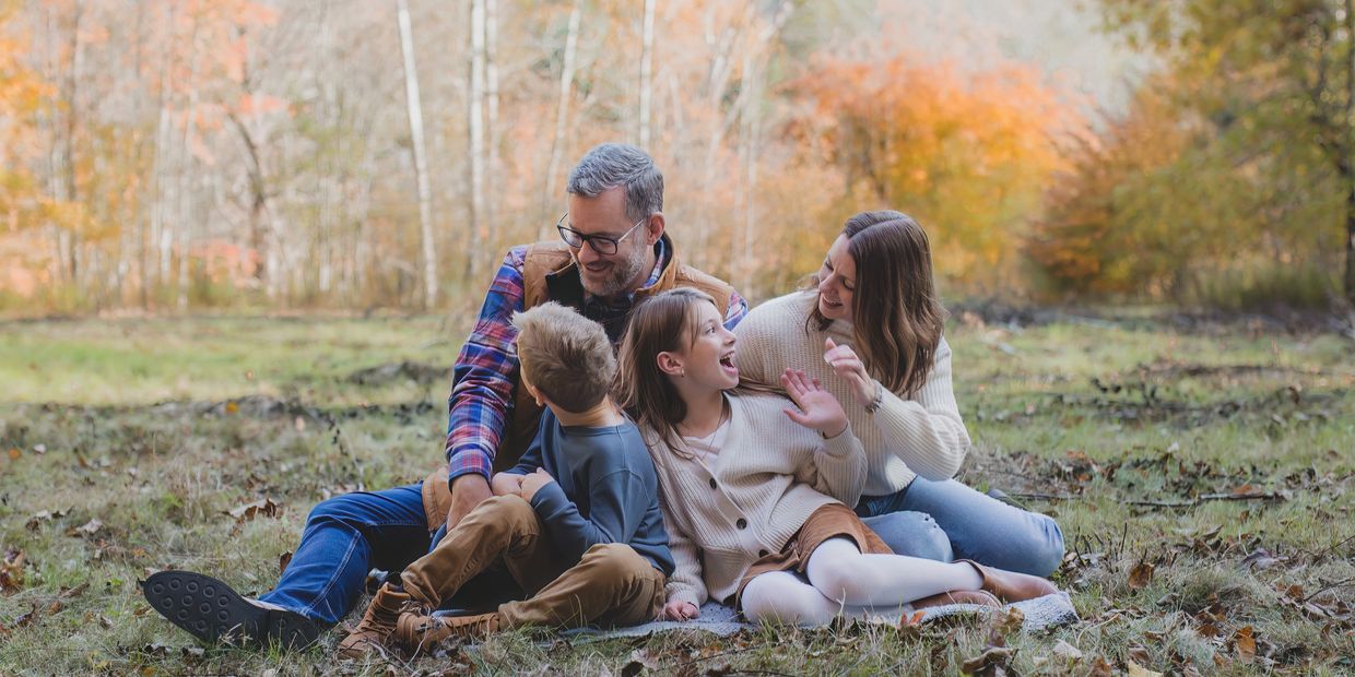 A happy family of four sitting and laughing outdoors in autumn.