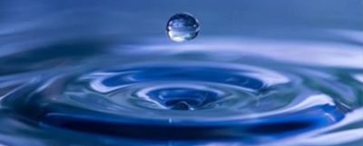 A water droplet suspended above rippling water surface.