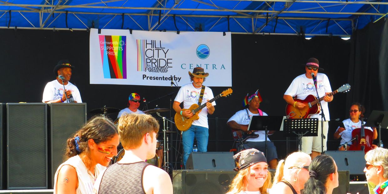 Band performing at Hill City Pride Festival under a colorful tent.