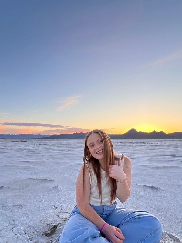 Young woman smiling and sitting on a salt flat at sunset.