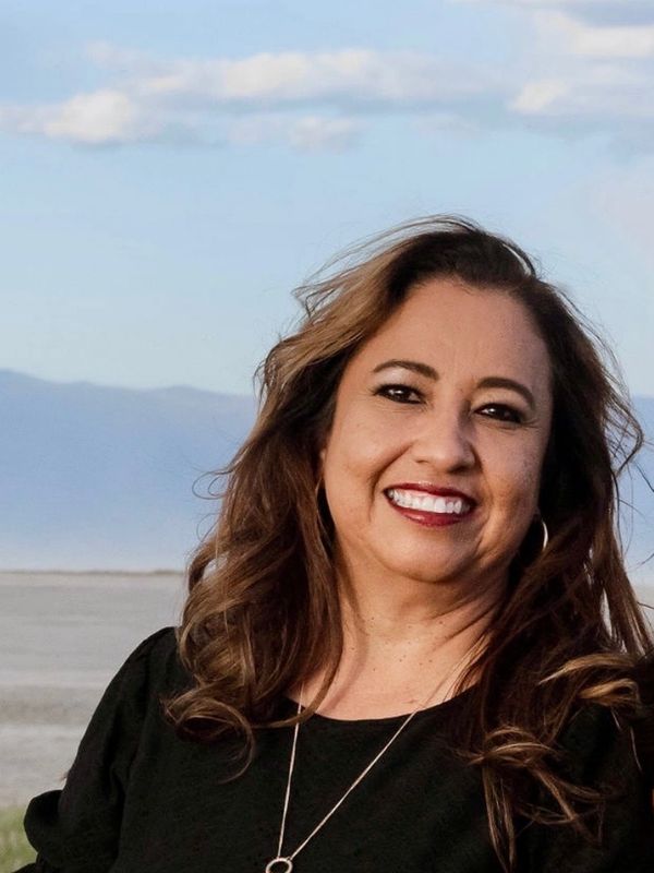 Smiling woman with wavy hair outdoors under a cloudy sky.