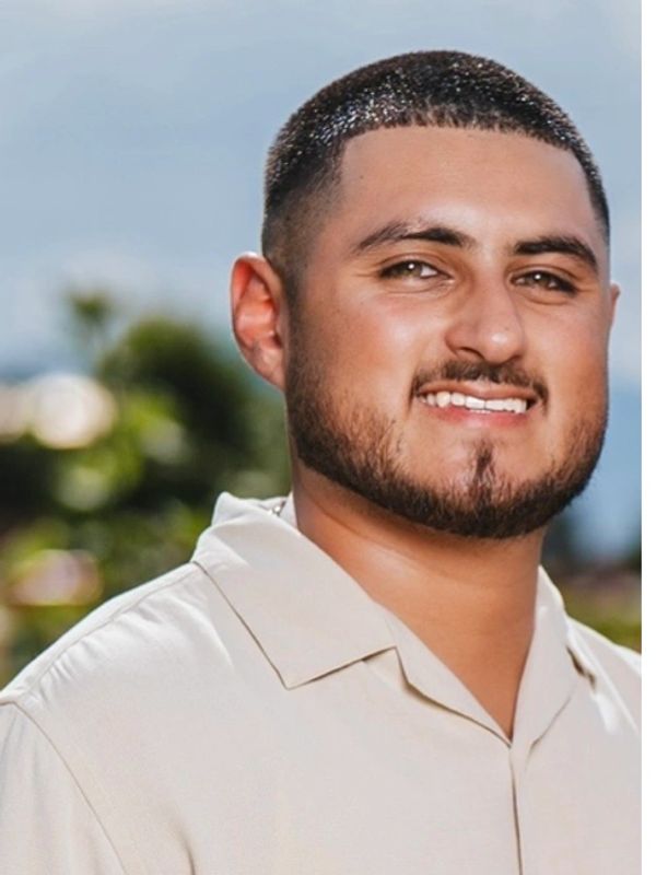Smiling young man with a beard outdoors in a light shirt.
