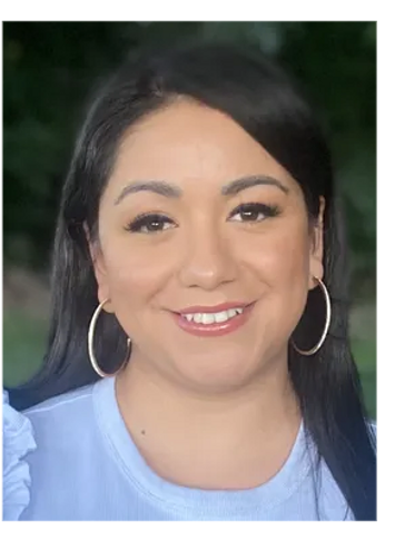 Woman with hoop earrings smiling outdoors.