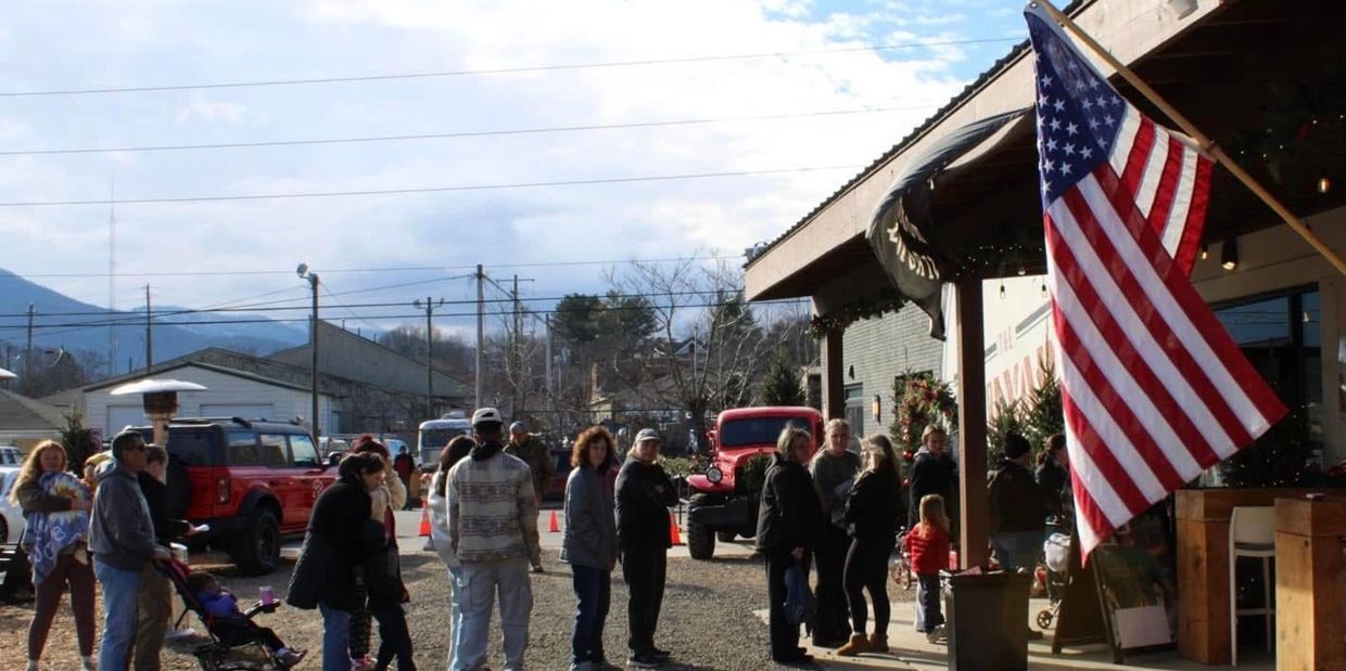 People standing in line outside a building with an American flag.