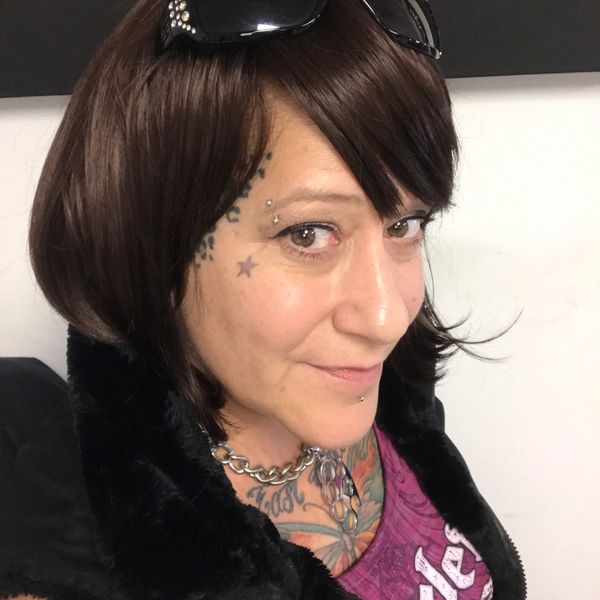 Woman with tattoos and piercings smiling, wearing sunglasses on her head.