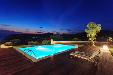 Lighted pool at dusk with wood decking and hillside view