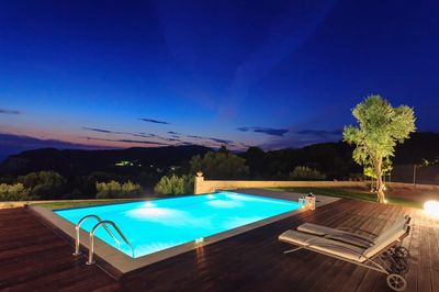 Lit pool with a wood deck overlooking the hills at dusk