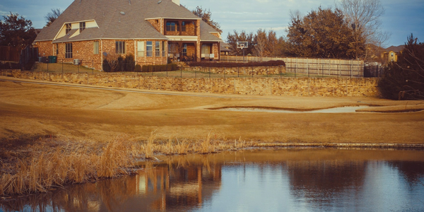 Large brick house with a pond and basketball hoop in the backyard.