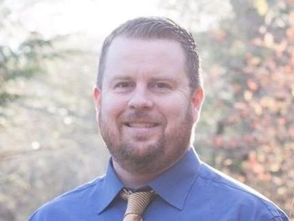 Smiling man in blue shirt and beige tie outdoors.
