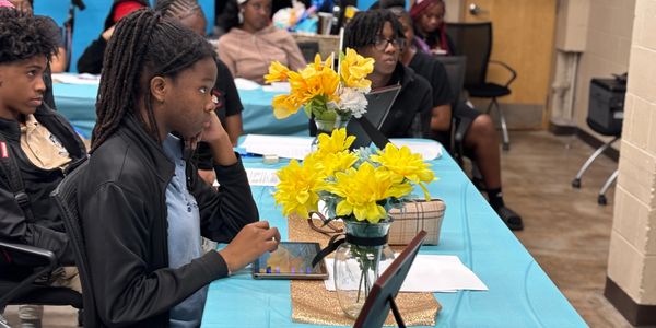 Students attentively participate in a classroom discussion around a table with yellow flowers.