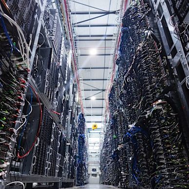 A corridor between tall server racks filled with cables in a data center.