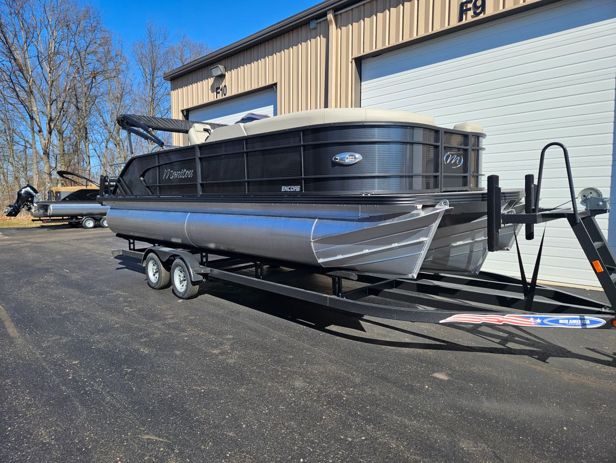 Black and gray pontoon boat on a trailer outside a building.