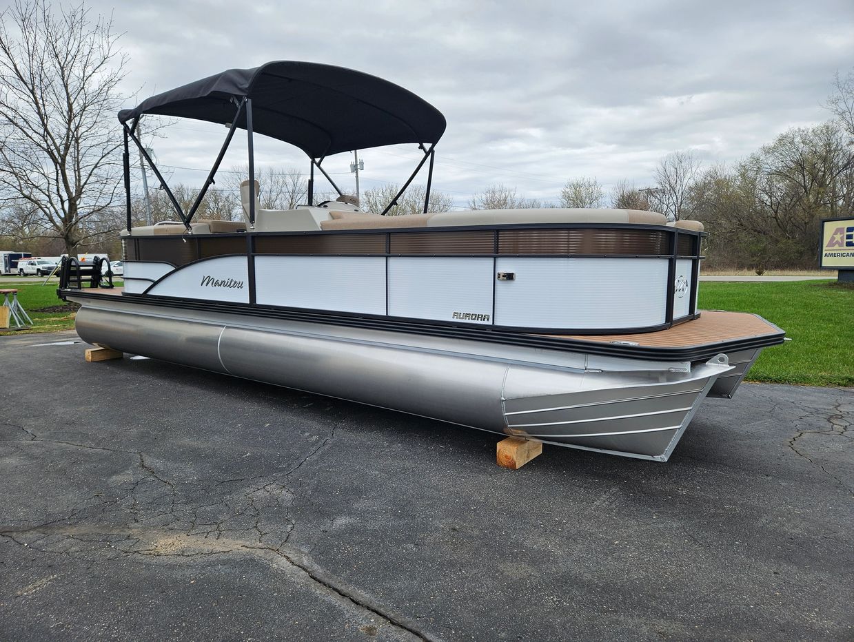 Silver and white pontoon boat on pavement with a black canopy.