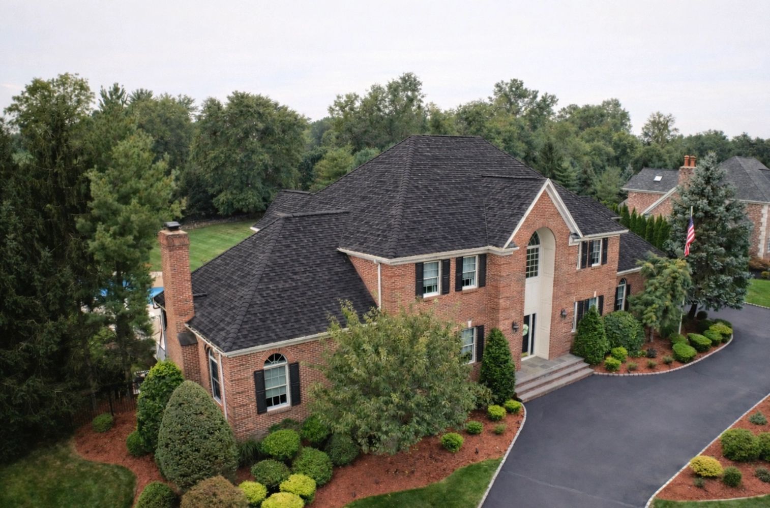 Elegant two-story brick house with black roof and manicured landscaping.