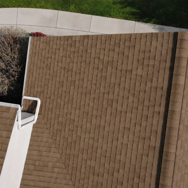 Aerial view of a brown shingled roof with a white chimney and surrounding greenery.