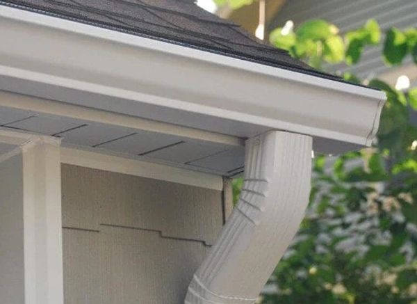 Close-up of a white rain gutter and downspout on a house corner.