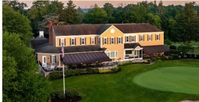 A large yellow clubhouse next to a green golf putting area at sunset.