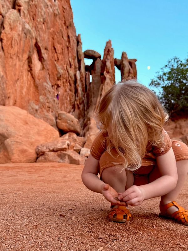 Child crouching and examining ground near red rock formations.