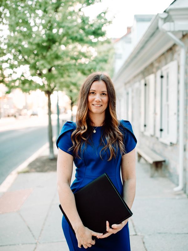 Woman in blue dress holding a folder on a sidewalk.