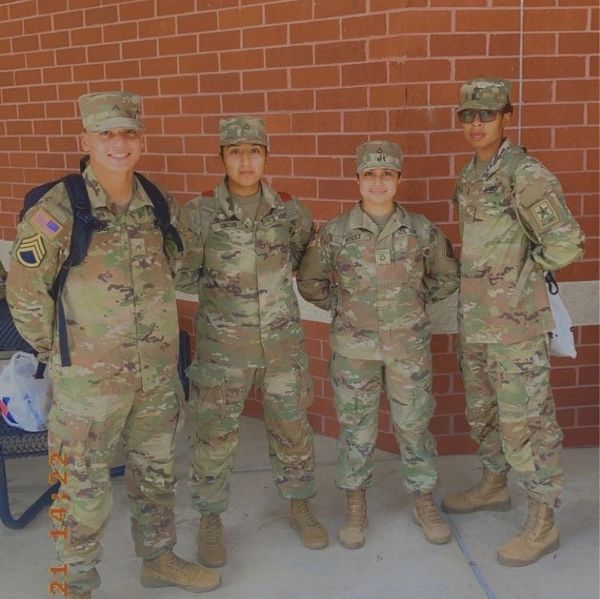 Four soldiers in camouflage uniforms standing in front of a brick wall.