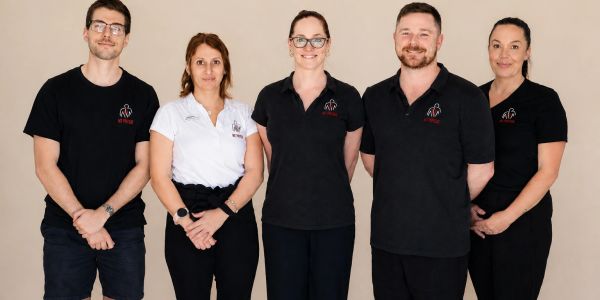 Five professionals posing for a photo against a plain background.