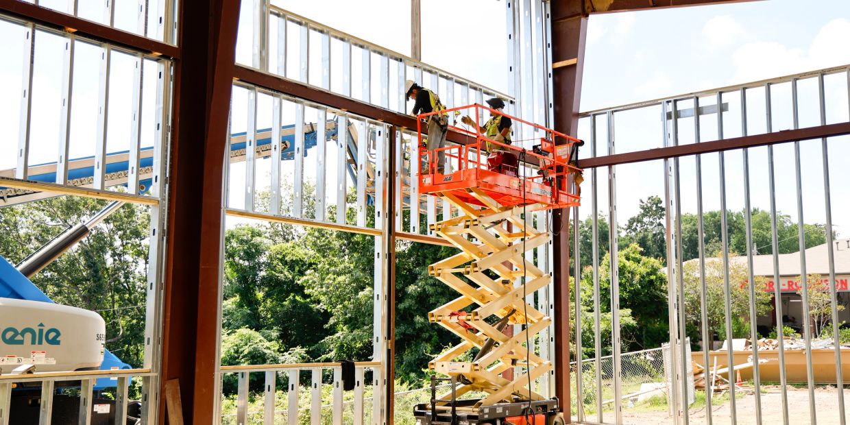 Workers on a scissor lift installing metal framing inside a building.